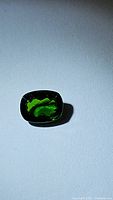 Photo of cushion cut natural chrome diopside gemstone on white background, showing deep electric green color and facets.