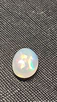 Close-up photo of the oval cabochon Ethiopian opal showing multicolored flashes on a black textured background.