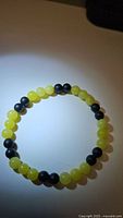 Photo showing natural black onyx and lemon jade beads patterned stretchy bracelet laid in a circle, illuminated in a dark environment.