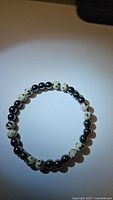 Top view of natural hematite and dalmatian jasper beaded bracelet on white surface.