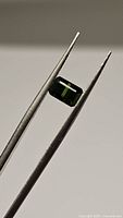 Close-up photo of a rectangular green tourmaline gemstone held with tweezers showing its clarity and cut from one angle.