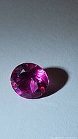 Close-up image of a round-cut hot pink topaz gemstone showing vibrant color and clarity.