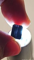 Close-up image showing rectangular emerald cut purple tourmaline held with fingertips against light source highlighting clarity and cut facets.
