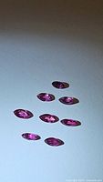 Eight marquis cut rubies in varying shades of fuchsia-pink to purple-red arranged on a flat surface under bright light showing clarity and cut.