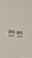 Pair of square cut transparent light pink rose quartz stones on beige surface