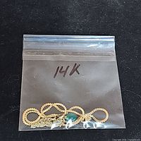 Clear plastic bag with coiled 14k gold chains and green teardrop pendant labeled '14K'
