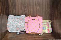Three cloth bags side by side on a wooden shelf: Longaberger floral handbag, Lily Bloom pink floral bag, Stone Mountain small floral crossbody bag