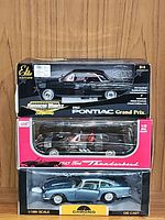 Three boxed diecast model cars in original packaging: Pontiac Grand Prix Elite Edition, Ford Thunderbird Metal Series, and Aston Martin DB5 Chrono metallic ice blue.