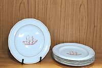 Stack of 7 dinner plates and 1 dessert plate showing red ship motif and scalloped edges with gold trim on white background