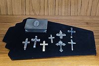 Seven cross pendants arranged on a black cloth with a vintage metal rosary box.