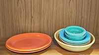 Stack of orange vintage Fiesta oval platters on left; stack of assorted bowls and yellow serving bowl on right.