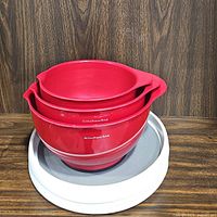 Nested set of three red KitchenAid plastic mixing bowls with spouts placed on a white plastic turntable with a gray surface.