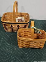 Two handmade woven wooden baskets, one larger spring basket and one smaller rectangular caddy basket, displayed on a green padded surface.