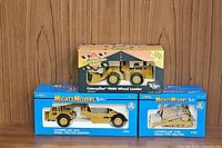Three Ertl Mighty Movers die-cast Caterpillar construction vehicle models in original packaging: 631E scraper, D10N tractor, 988B loader