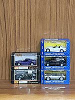 Five Maisto diecast model cars stacked and boxed, showing various shades including white, black, blue, and gray. Packaging indicates features like diecast metal, pull back action, opening doors, and plastic interiors.