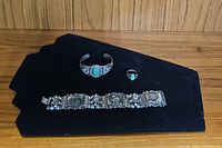 Three pieces of jewelry on black background: panel bracelet, cuff bracelet, ring