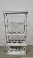 Front view of the white 4-tier plastic utility storage shelf showing all shelves evenly spaced.