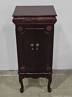 Front view of closed vintage wooden jewelry armoire with carved details and two cabinet doors with metal handles.