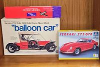 Boxes of three vintage model kits including the Rolls Royce Silver Ghost balloon car and Ferrari 275 GTB car models displayed on a wooden shelf.