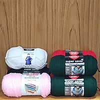 Photo showing four yarn bundles: white Impeccable, pink Value Economique, and two green and red Super Saver Red Heart yarns.