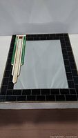 Front view of the rectangular mirror showing the decorative slag glass border with black tiles and multiple colored slag glass pieces in an Art Deco style.