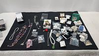 Overview of assorted costume jewelry necklaces and small jewelry pieces spread on a black cloth, including beaded and chain necklaces plus boxed items.