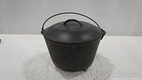Full front view of black cast iron cauldron with lid closed, showing bail handle and round shape.
