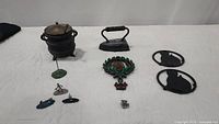 Collection including cast iron cauldron, cast iron iron, decorative wreath, two cast iron trivets, and metal figures on agate stones, plus pewter figure