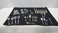 Wide view of all flatware and utensils on black cloth, showing knives, forks, spoons, and serving utensils.
