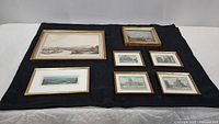 Full view of all 7 gold framed landmark prints laid out on black cloth showing variety of sizes and framing styles.