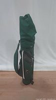 Green golf carrying bag standing upright, fully zipped and closed with shoulder strap visible