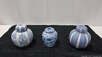 Three blue and white ceramic ginger jars of varying sizes arranged side by side on black cloth.