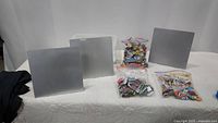 Three square silver metal magnetic display boards set up in a row, three plastic bags of assorted magnets placed in front.