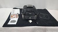 Ninja Foodi Grill with power cord, black grilling basket, instruction manuals, and recipe guide displayed on black cloth.