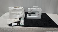 Full lot photo showing sewing machine, foot pedal, carrying bag, instruction manual, accessories and mat