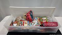 Plastic tote filled with various Christmas gift wrapping supplies including bags, bows, and tags.