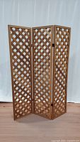 Full view of the wooden trifold lattice room divider standing open with three panels.