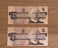 Front view of two 1986 Canadian $5 bills showing Sir Wilfrid Laurier portrait and denomination details.