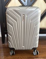 Front view of the silver expandable carry-on luggage with geometric ridges and four double spinner wheels.