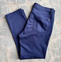Folded pair of dark blue cotton pants laid flat to show front and back pockets and overall fabric texture in natural light.