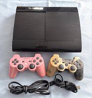 Overall photo of Sony PS3 Super Slim console, two wireless controllers in pink and gold/black, plus cables.