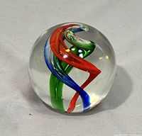 Front-facing image of the clear glass paperweight showing red, green, and blue internal swirling ribbons.