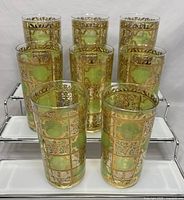 Set of eight vintage mid century Culver Prado highball glasses arranged on a rack showing green squares with gold scroll patterns