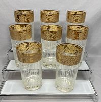 Eight Culver Tyrol highball glasses arranged on a white tiered stand showing the etched gold bands and clear glass with vertical etched lines
