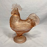 Front view of pink pressed glass rooster-shaped candy dish lid showing detailed feather pattern and translucent pink glass.
