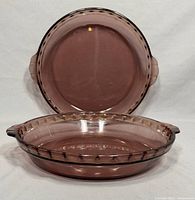 Two purple amethyst Pyrex glass pie plates arranged with one plate upright and the other laying flat showing the inside and decorative rim detail.