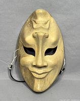 Front view of the comedy face mask showing smiling carved features in light wood with natural grain.