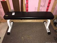 Front view of the flat workout bench showing black cushioned top and white metal frame.