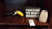 Photo showing wooden toucan bird figurine, family quote sign, and stone candle holder on a wooden shelf.