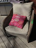 Front view of wicker chair showing seat and back cushions plus pink throw pillow
